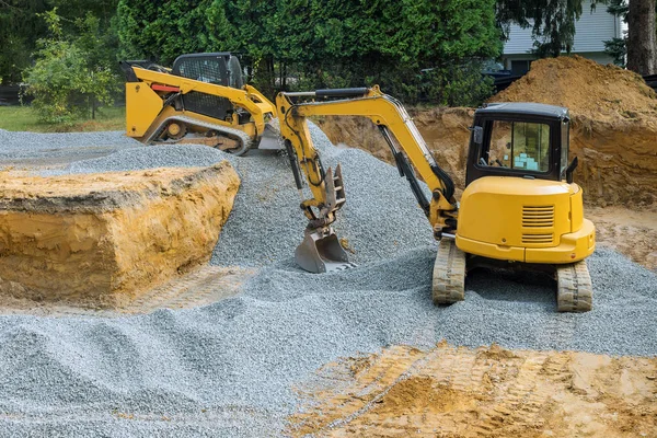 Una excavadora sobre ruedas relleno de los trabajos de cimentación en el sitio de construcción para el edificio en construcción . — Foto de Stock