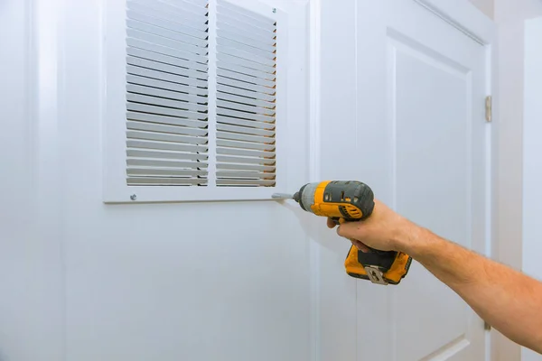 Man is holding hand drill in hands. Worker installing the wall vent works renovation in the flat.