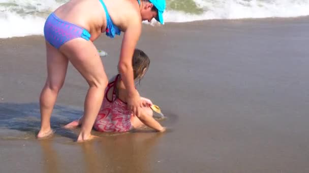Mother rubs her daughter with a tanning cream on the shore of the ocean — Stock Video