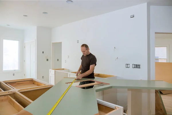 Mies käyttää mittanauhaa puisen työtason koon mittaamiseen modernissa keittiössä kodin parantamiseksi . — kuvapankkivalokuva