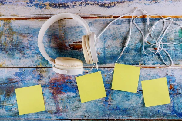 Gelbe Haftnotizen leere quadratische Erinnerung mit weißen Kopfhörern auf Musikkonzept, im blauen alten Holzhintergrund — Stockfoto