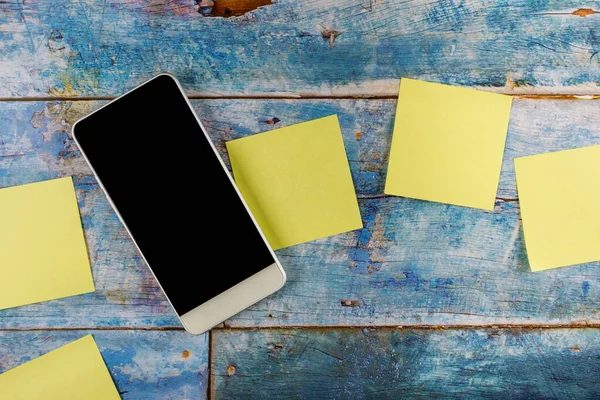 Sarı yapışkan notlar boş kare hatırlatıcı ile mavi ahşap arka planda akıllı telefon