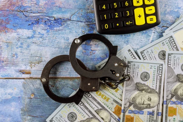 Contabilità finanziaria criminale con calcolatrice e manette della polizia su un mucchio di banconote da cento dollari — Foto Stock