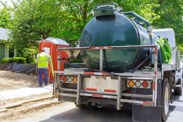 Sewage truck on worker pumping feces out of rental toilet for disposal and cleaning at the construction