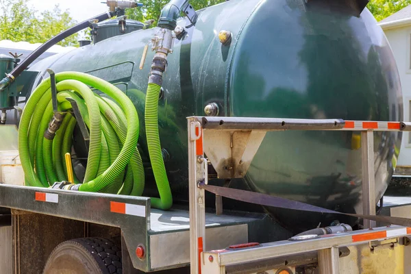 Sewage tank truck pumping machine cleaning a rental mobile toilet with water hose