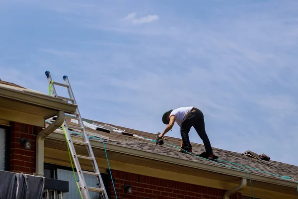 Construction worker roofer builder on roof structure applying asphalt shingles on roofing