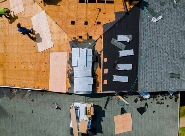 A roofer nailing shingles with air gun, replacing roof cover protection being applied, apartment development