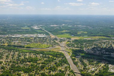 Yazın yeşil tarlalar arasında sıralı binalar ve kıvrımlı sokaklar olan bir kasaba köyünün üstündeki beyaz bulutların hava manzarası.