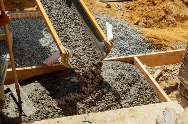 İnşaat işçisi inşaat alanında el arabası ve çimento ve çakıl döken karıştırıcı kamyonla beton işlerinde kaldırım için çimento döküyor.