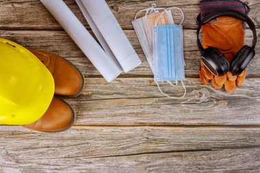 Endüstri işçisi koruyucu ve cerrahi maske, kulaklık iş giysisi güvenlik botları deri eldivenler ofis koronavirüs salgını kovid-19 'un planlarıyla çalışan mimarlara sarı şapka.,