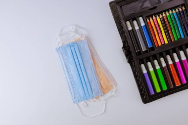 Sanat okulu malzemeleri için renkli kalemler. Güvenli okul koronavirüsü COVID-19 salgın tıbbi hijyen maskeleri.