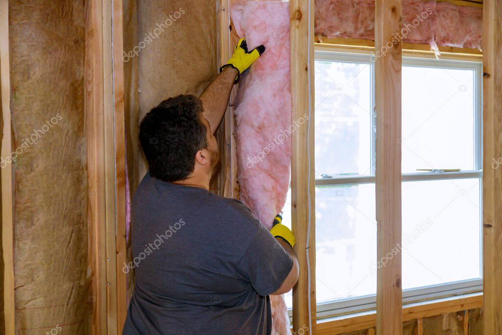 Construction worker thermally insulating insulation layer under house with glass wool