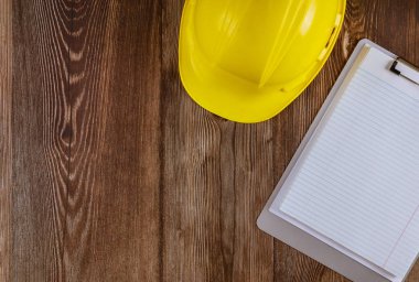 Ofis masasında boş defterle çalışan mühendis ahşap masada koruyucu sarı kaskla çalışıyor.