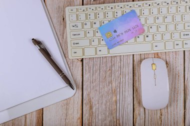 Çevrimiçi ödeme kartını açık defter ahşap ofis masası olan bir klavye ile kavra.