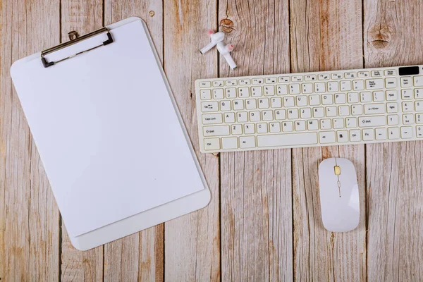 Office table with blank notebook and computer keyboard on a wooden table background.