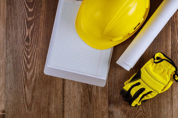 Architect or engineer working on blueprint architecture mode in office notepad on yellow safety helmet on background.