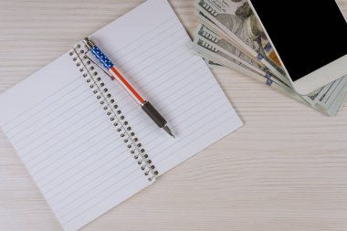 Boş sayfaları olan bir defter akıllı telefon çalışma alanı ofis malzemeleri ve bize dolar veren bir kalem.