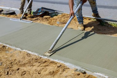 Worker plastering the concrete cement during construction contractor using a float to sidewalk clipart