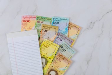 Üzerinde farklı banknotlar olan ofis masası. Venezuela Bolivar. Boş bir not defteri.