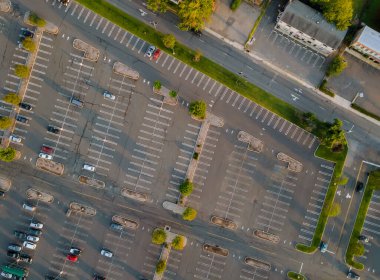 Alışveriş merkezinin yakınındaki bir otoparkta beyaz şeritler ve kaldırımlarla bölünmüş çok sayıda farklı markalı arabanın hava görüntüsü.