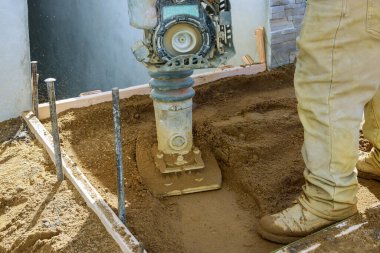 Titreşim plakalı sıkıştırıcı ile çalışan işçiler yeni bir kaldırım inşa ediyorlar.