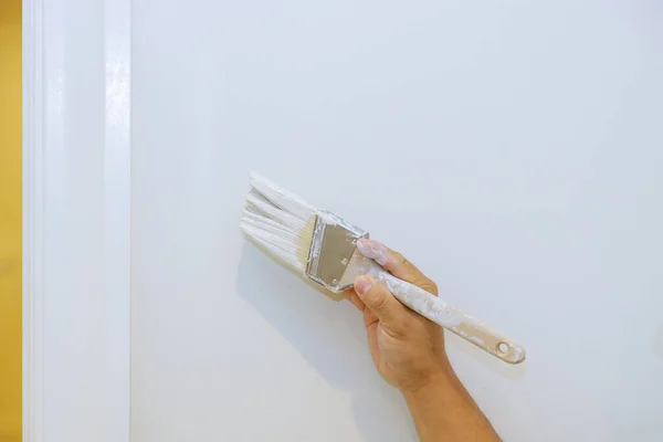 Worker are painting in the door trim molding on a white wall renovating house interior