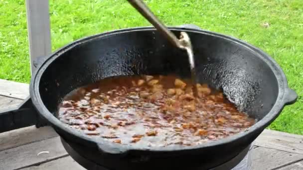 Cozinhar pilaf uzbeque real durante um cozinheiro mexe carne com colher de ferro que cozido no caldeirão em chamas — Vídeo de Stock