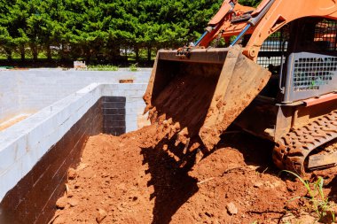 İnşaat traktörü iş günlerinde ağaçlarla çevrili binanın temelini kirletiyor..