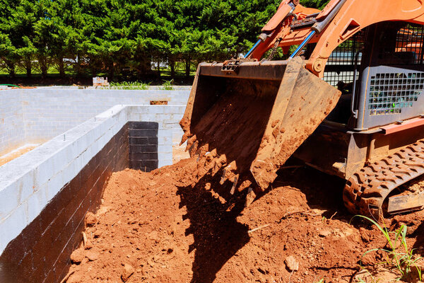 Строительный трактор сбрасывает грязь в фундамент здания, окруженный деревьями в рабочий день.