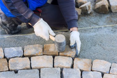 İşçi, iş gününün altında inşaat alanında yol yaparken taşları dikkatlice yerleştirir.