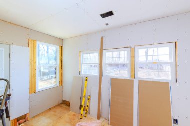 Alçıpan üç pencereli mesken odasına monte ediliyor. Doğal ışık ve bitmemiş döşemeler sergileniyor..