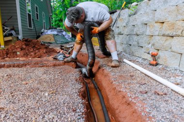 İnşaat işçisi iş günü evin arkasındaki hendeğe drenaj borusu yerleştiriyor..