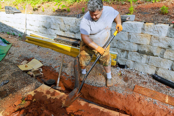 Рабочий использует лопату, чтобы вырыть траншею в саду для нового проекта дренажной системы на открытом воздухе в рабочий день.