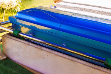 Parlak mavi tabut, huzurlu mezarlıktaki anma töreninde yeşilliklerle çevrili sedyeye konur.