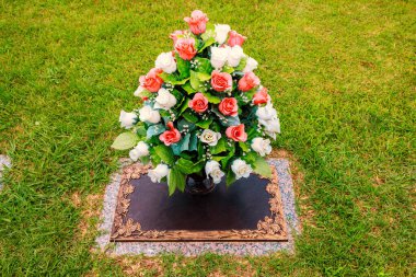 Beyaz, pembe güllerin düzenlenmesi huzur dolu mezarlıkta veda töreninde mezar taşını süslüyor.