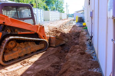 İnşaat kazıcısı, banliyö bölgesinde iş gününün altındaki binanın yanında siper kazıyor.