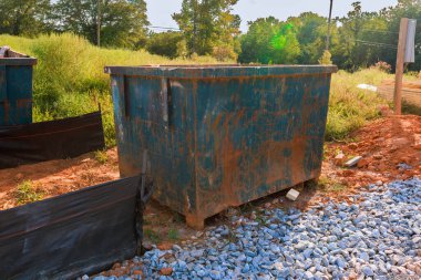 İnşaat alanındaki paslı çöp konteynırının etrafı iş günlerini yansıtan kayalarla çevrili..