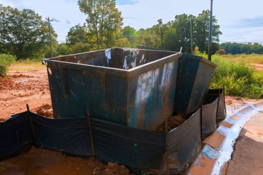 İki büyük enkaz konteyneri iş günü ağaçların ve çamurlu zemin arasında şantiyenin yanında duruyor..