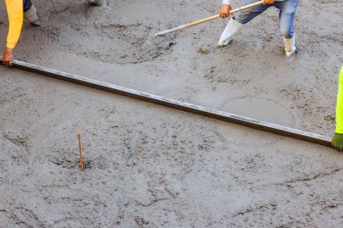 İnşaat işçileri betonu düzleştirmek için uzun metal aletler kullanarak yeni dökülmüş betonu düzleştiriyorlar.