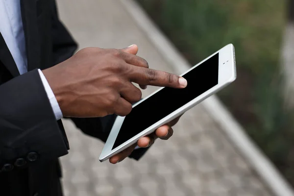 Top close up view of young african american male hand and sleeve hold white tablet pc and scrolling down the page of website. Mock up image of man using gadget for working on small business.