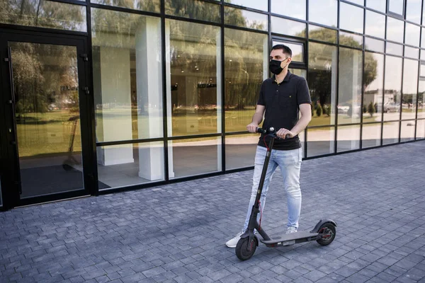 Genç kızın tam boy portresi elektrikli scooter 'da, scooter' da veya e-scooter 'da. Adam kendini ofis binasının yanında duran ikinci bir kovandan korumak için maske takıyor. Şehir ulaşımı.