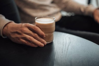 Kafede otururken el ele tutuşan bir adamın sıcak kahve fincanını yakın plan çek. Bekar küçük işletme sahibi sabah rutini, planlama. Latte, americano, capuccino, espresso konsepti..  
