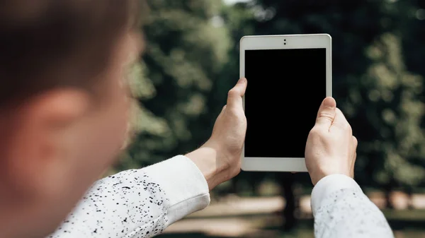 Close up shot of hands hold white tablet pc in the park. Software tester is trying to find a 5G network. Mock up image of gadget with blank black screen. Man is looking for a road on the navigator.