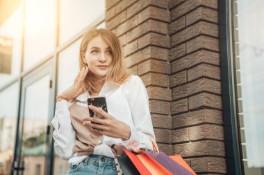 Çekici bir bayanın seçici odak noktası. Bir sürü çanta, telefon, alışverişçi, güneş gözlüğü, beyaz gömlek, yeni kıyafetler, alışveriş paketleri, perakende satış mağazası, siyah cuma konsepti.