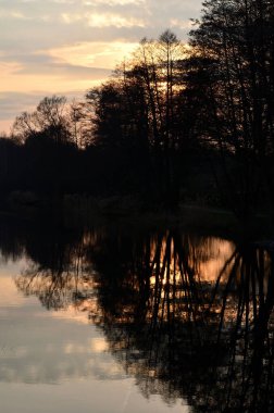 Seddin üzerindeki ağaçlar gün batımında suya yansıyor.