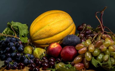 Taze üzümler, bir altın kavun, olgun şeftaliler, koyu incirler ve kırsal bir ahşap masa üzerine dizilmiş parlak kirazlar da dahil olmak üzere çeşitli meyvelerden oluşan canlı bir hayat.