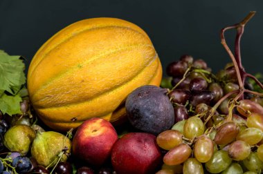 Taze üzümler, bir altın kavun, olgun şeftaliler, koyu incirler ve kırsal bir ahşap masa üzerine dizilmiş parlak kirazlar da dahil olmak üzere çeşitli meyvelerden oluşan canlı bir hayat.