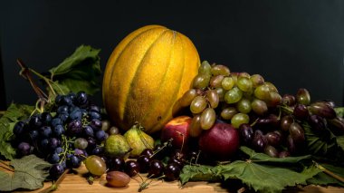 Taze üzümler, bir altın kavun, olgun şeftaliler, koyu incirler ve kırsal bir ahşap masa üzerine dizilmiş parlak kirazlar da dahil olmak üzere çeşitli meyvelerden oluşan canlı bir hayat.