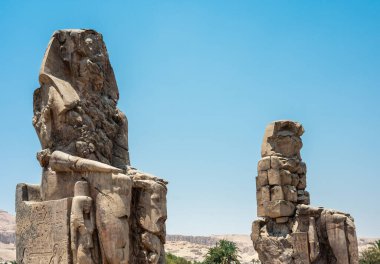 Luxor, Mısır - 27.07.2025. Memnon Colossi olarak bilinen iki devasa taş heykel Nil Nehri 'nin batı kıyısında arka planda kayalık bir dağ sırasına sahip uzun boylu dururlar.
