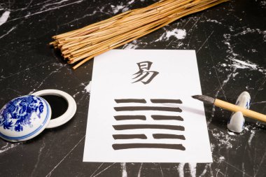 Close up of an I Ching arrangement with the 63th hexagram (After Completition/Chi Chi) written with a chinese ink brush on rice paper. There are also yarrow stalks, and a chinese ink tank on black marble. clipart